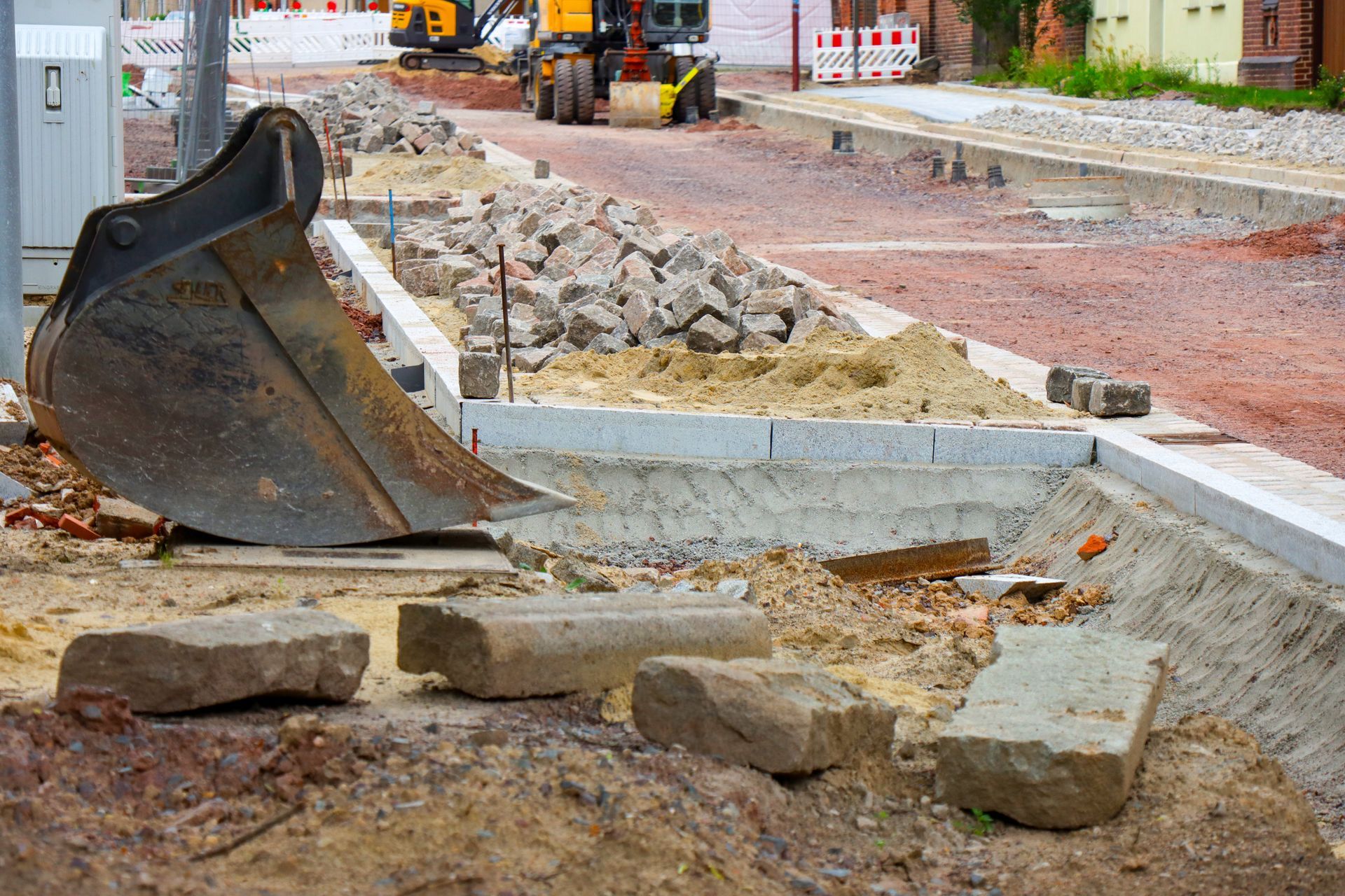 Baustelle mit einem Bagger, einer ausgehobenen Fläche und Steinblöcken.