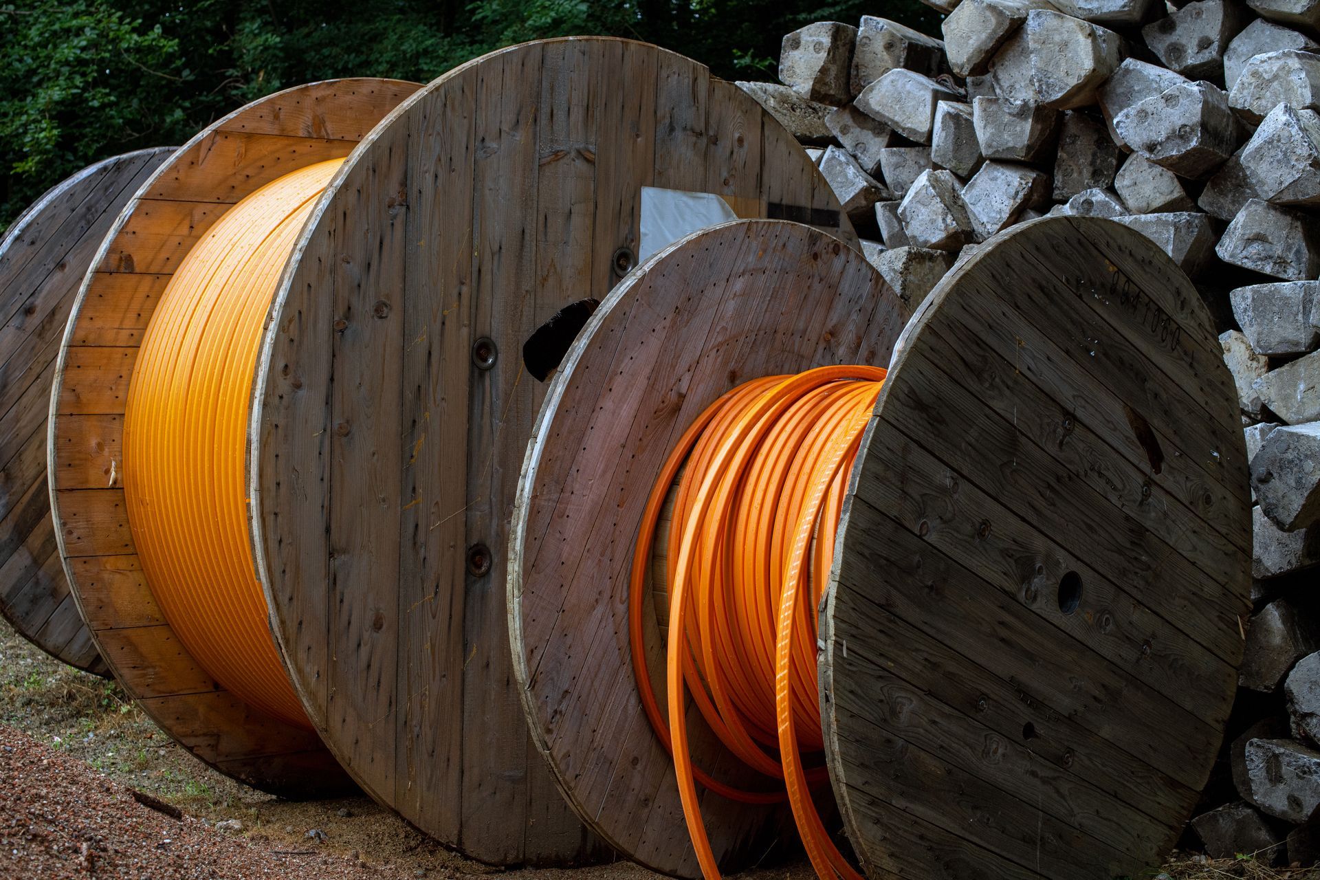 Holzspulen, gefüllt mit orangefarbenem Kabel, im Freien neben einem Holzstapel gestapelt.