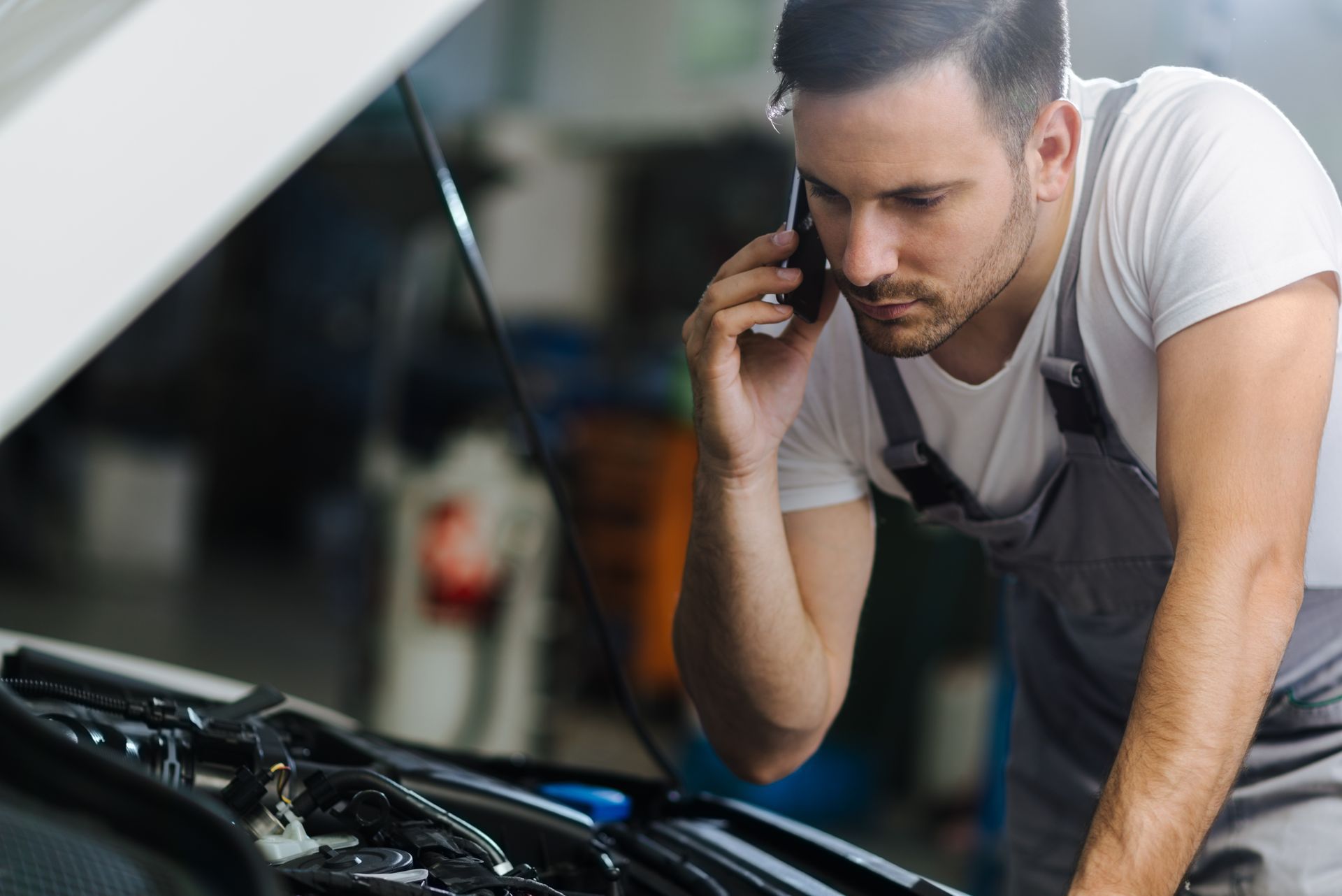 Mécanicien au téléphone devant le capot ouvert d'une voiture