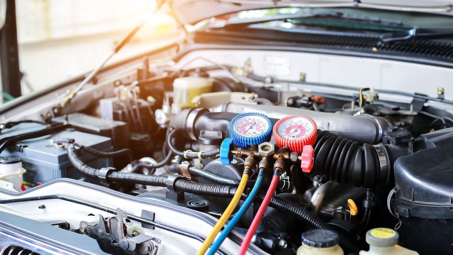 Moteur de voiture avec jauges attachées, probablement pour une réparation de climatisation.