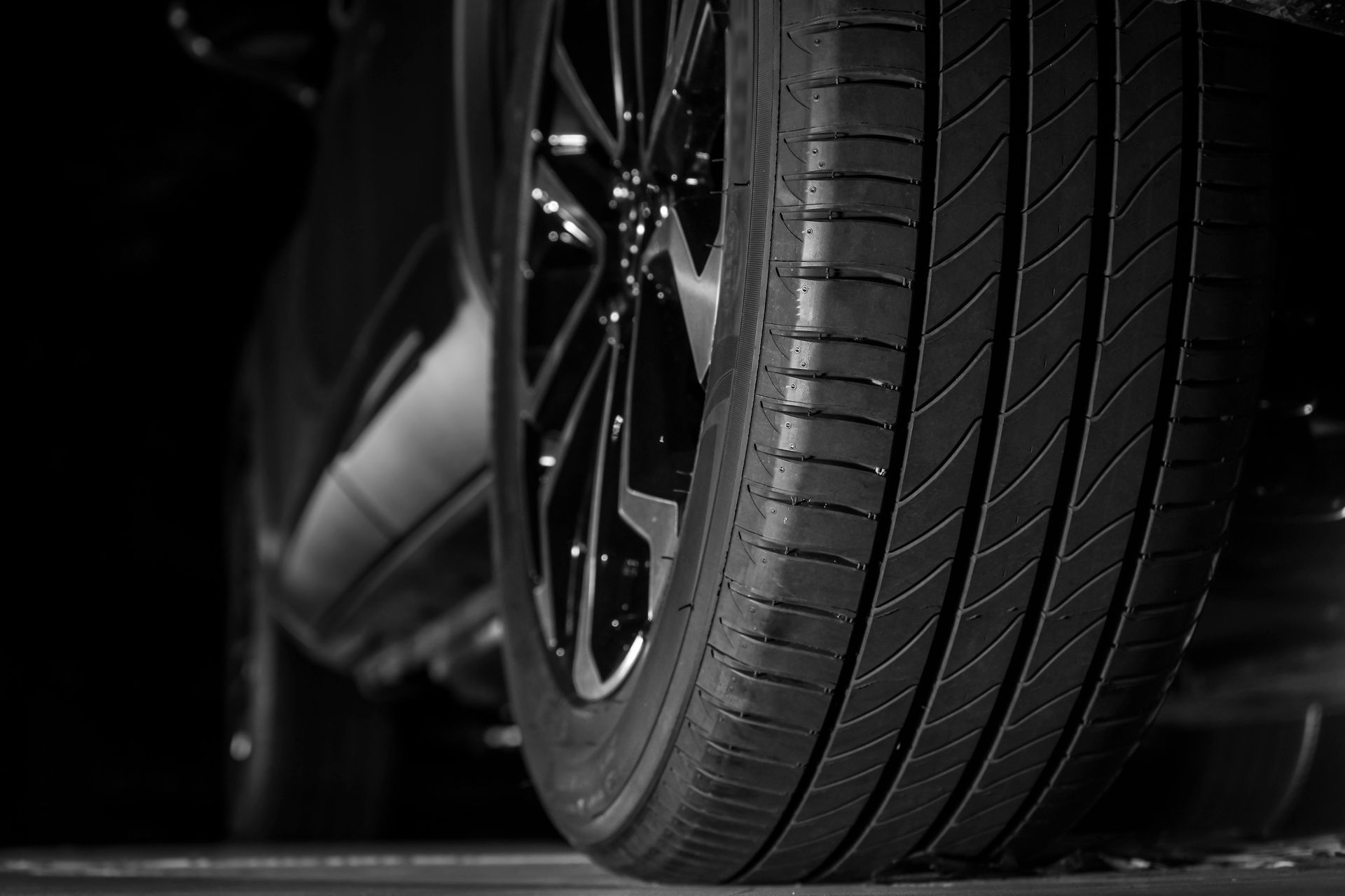 Gros plan noir et blanc d'un pneu et d'une jante de voiture. Détail de la bande de roulement visible, positionné sur une surface sombre.