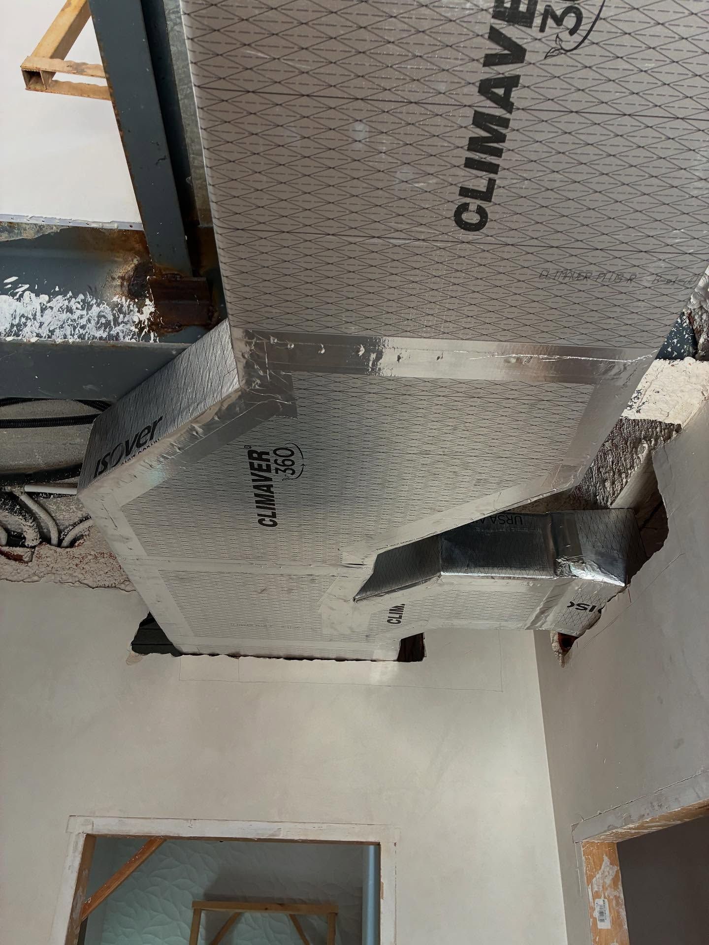 Conductos aislados y estructura del techo a la vista sobre una habitación interior y una puerta.