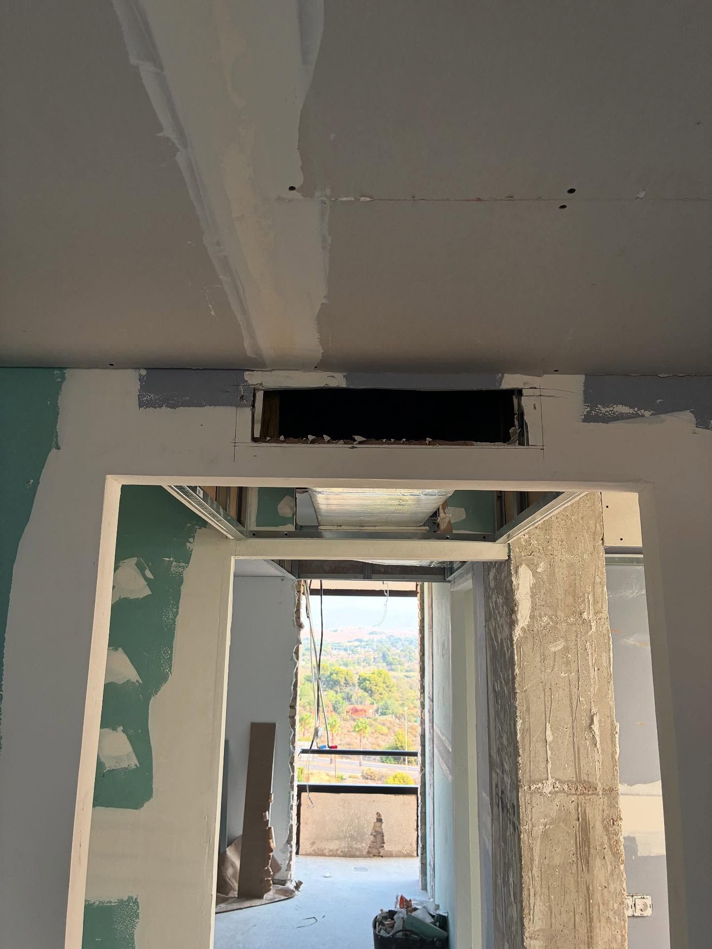 Pasillo estrecho con paredes de yeso sin terminar y una abertura rectangular que da a una ventana luminosa al fondo.