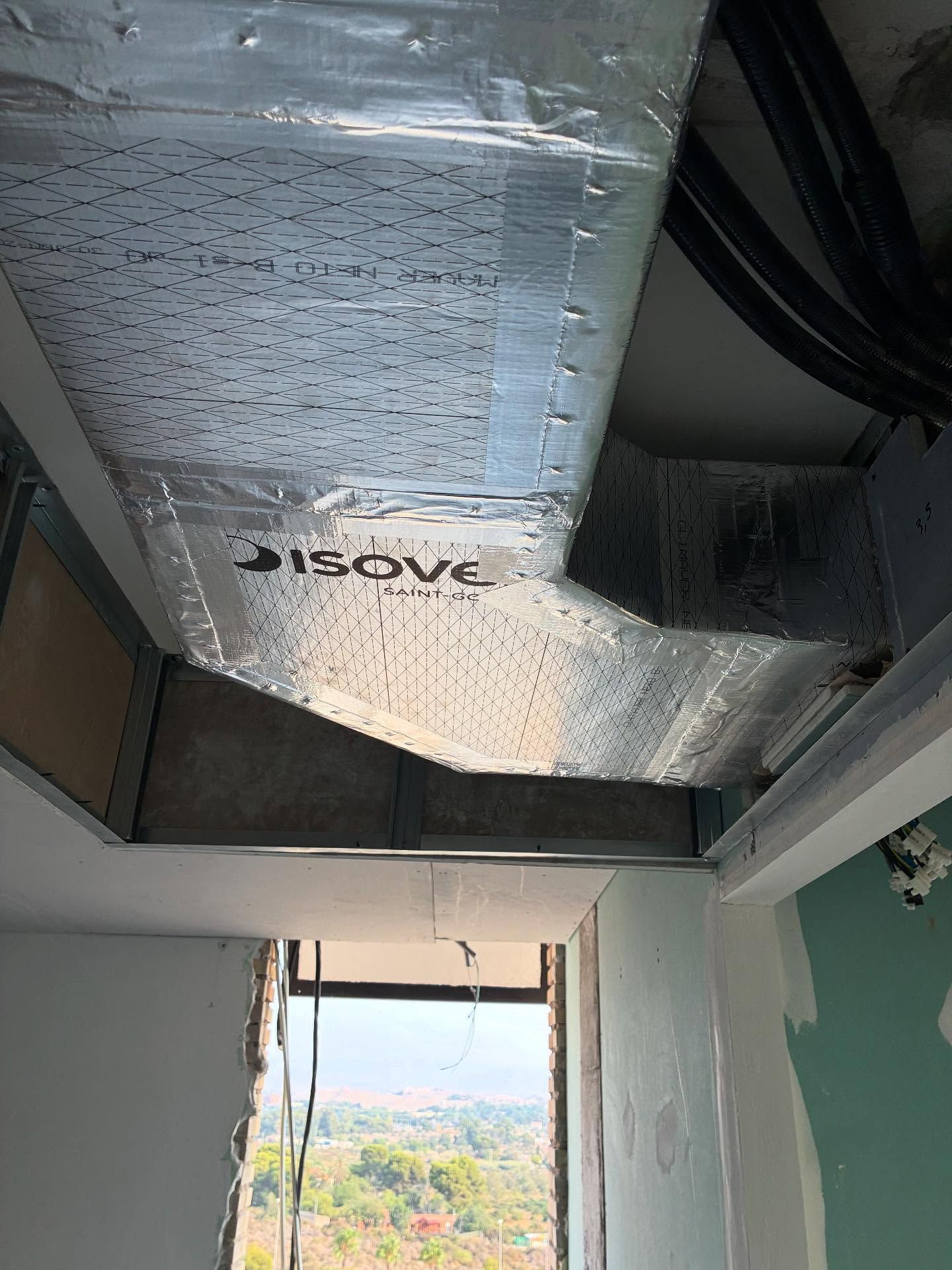 Conductos plateados de climatización en una abertura del techo de una habitación, con luz natural visible 