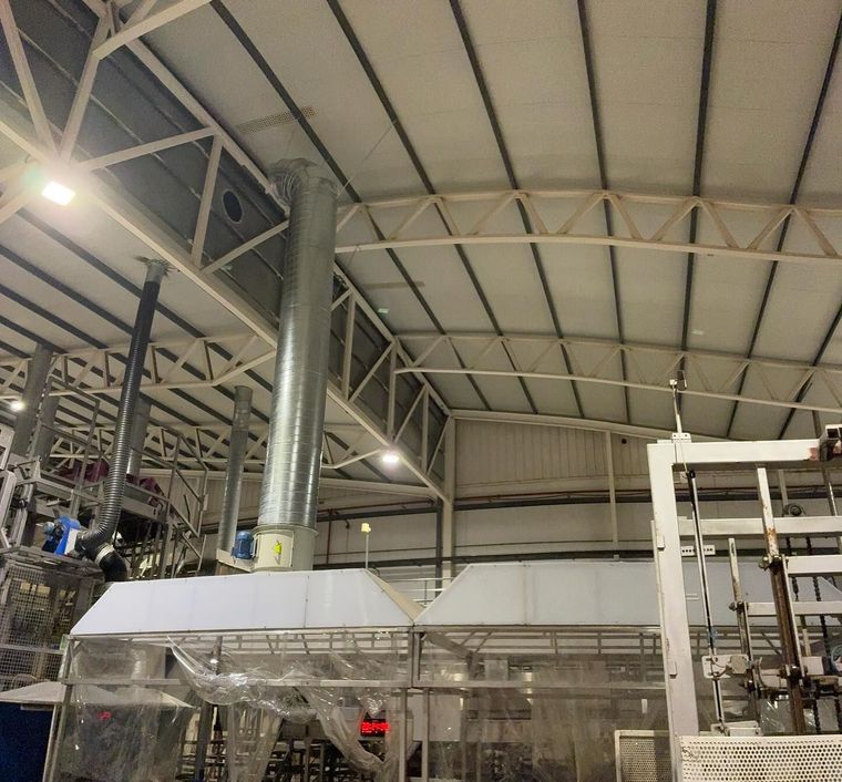 En el interior de una fábrica, grandes máquinas metálicas y conductos bajo un techo industrial alto