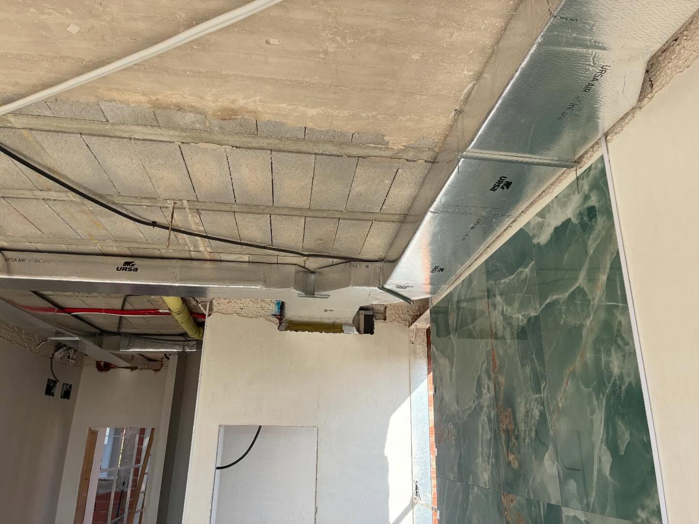 Habitación parcialmente terminada, con el techo de hormigón a la vista, cables expuestos y un panel de pared 