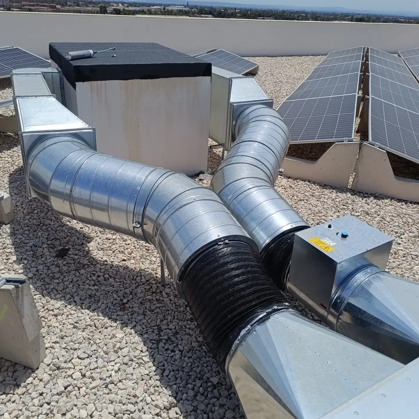 Conductos de ventilación de climatización en la azotea y tuberías plateadas junto a paneles solares sobre un tejado de grava