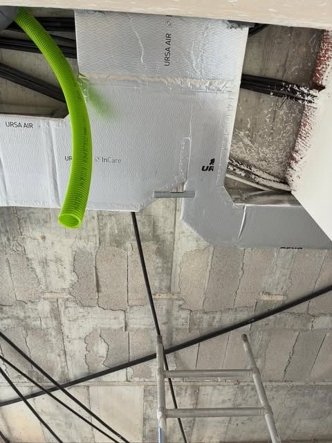 Aislamiento del techo, conductos expuestos y escalera metálica en un espacio de servicio sin terminar
