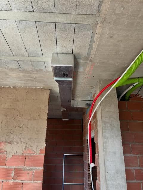 Parte inferior de un techo de hormigón, con conductos metálicos por encima de una pared de ladrillo