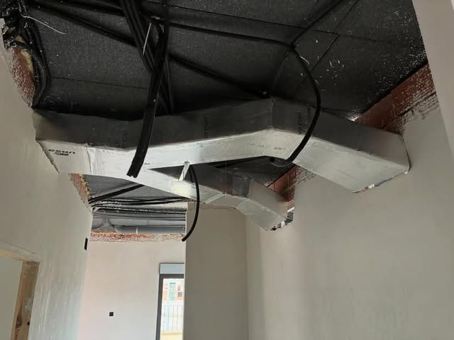Conductos de ventilación plateados a la vista y cables negros colgando de un techo oscuro sin terminar