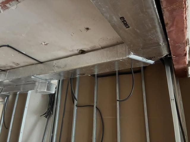 Techo a la vista con aislamiento, cables colgantes y placas de yeso sin terminar en una zona en obras