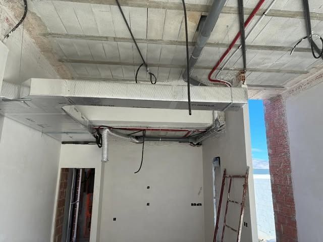 Interior parcialmente terminado, con vigas del techo expuestas, cables colgantes y paredes blancas