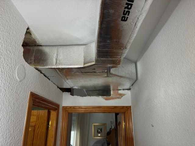 Techo de pasillo estrecho con conductos y rejillas de ventilación a la vista sobre las puertas de madera.