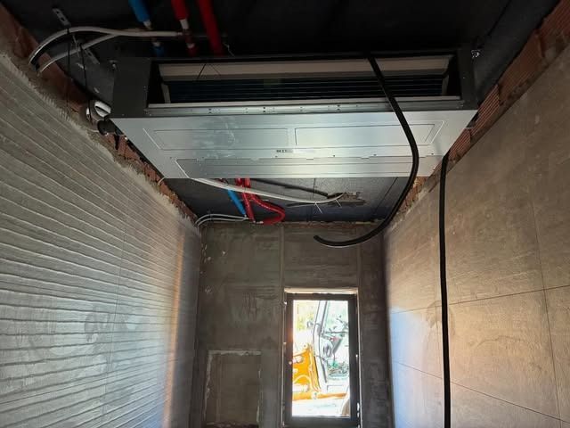 Pasillo en obras con conductos y cables a la vista en el techo, y una puerta al fondo.