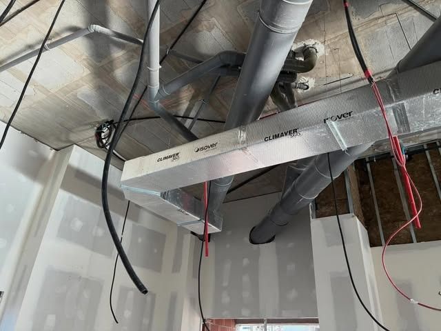 Conductos de climatización y cables colgantes a la vista en una habitación interior sin terminar.