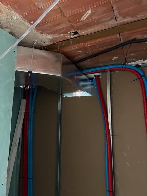 Techo a la vista con cables eléctricos rojos y azules colgando, sobre paneles de yeso sin terminar y aislamiento térmico