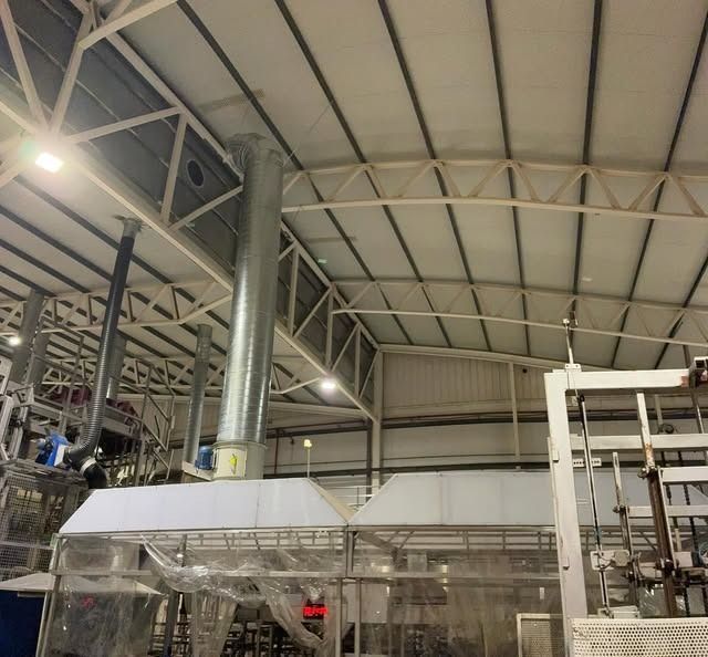 Interior de una gran fábrica industrial, con conductos y tuberías metálicos, maquinaria y vigas en el techo alto