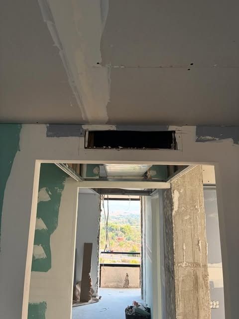 Pasillo renovado con placas de yeso sin terminar, una abertura en el techo y una puerta que da a una habitación