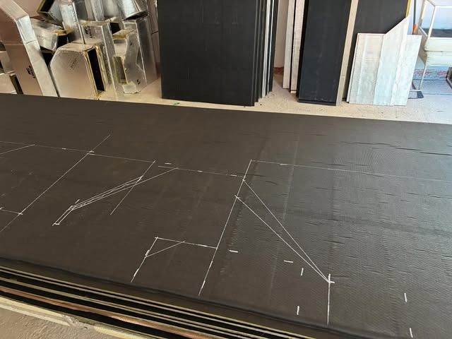 Baldosas negras colocadas en el suelo de una tienda o taller, con pilas de materiales al fondo.