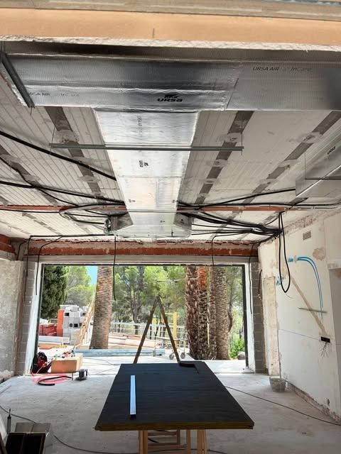 Garaje parcialmente renovado, con el techo a la vista, cables colgantes y una mesa de trabajo junto a una puerta abierta