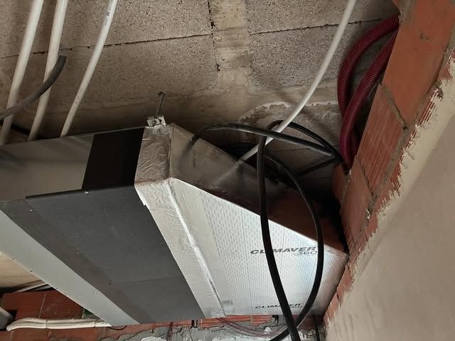 Primer plano de un conducto metálico de climatización y unos cables en la esquina de un techo sin terminar