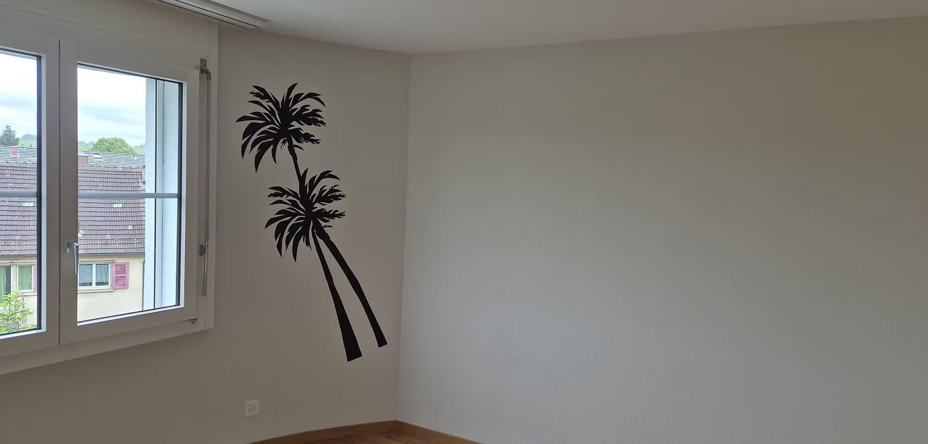 Leeres Zimmer mit Fenster und einem schwarzen Palmen-Wandtattoo an einer weissen Wand