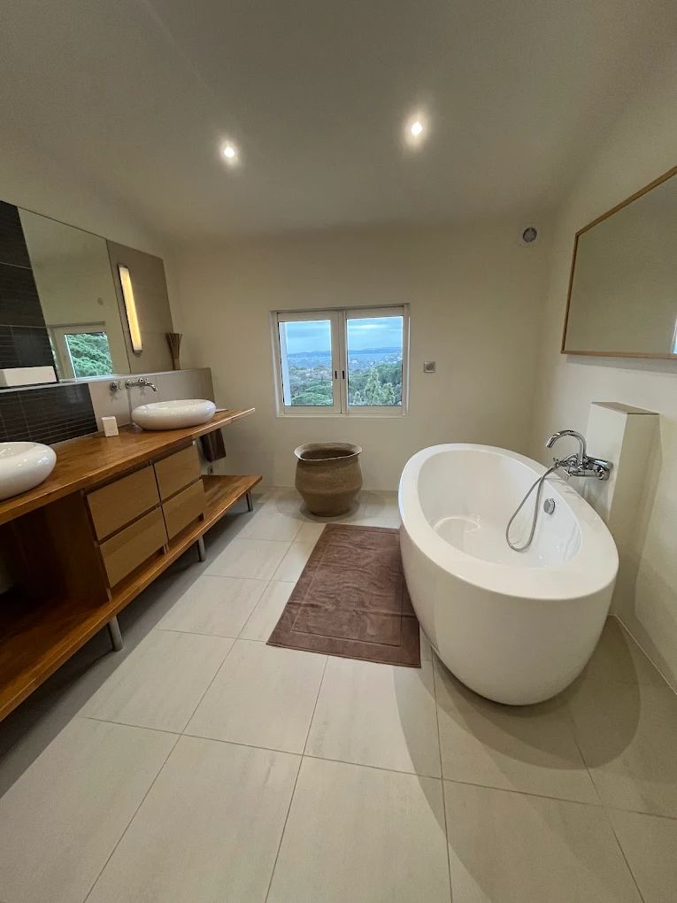 Salle de bains moderne avec baignoire îlot, double vasque, grand miroir et vue sur l'extérieur.
