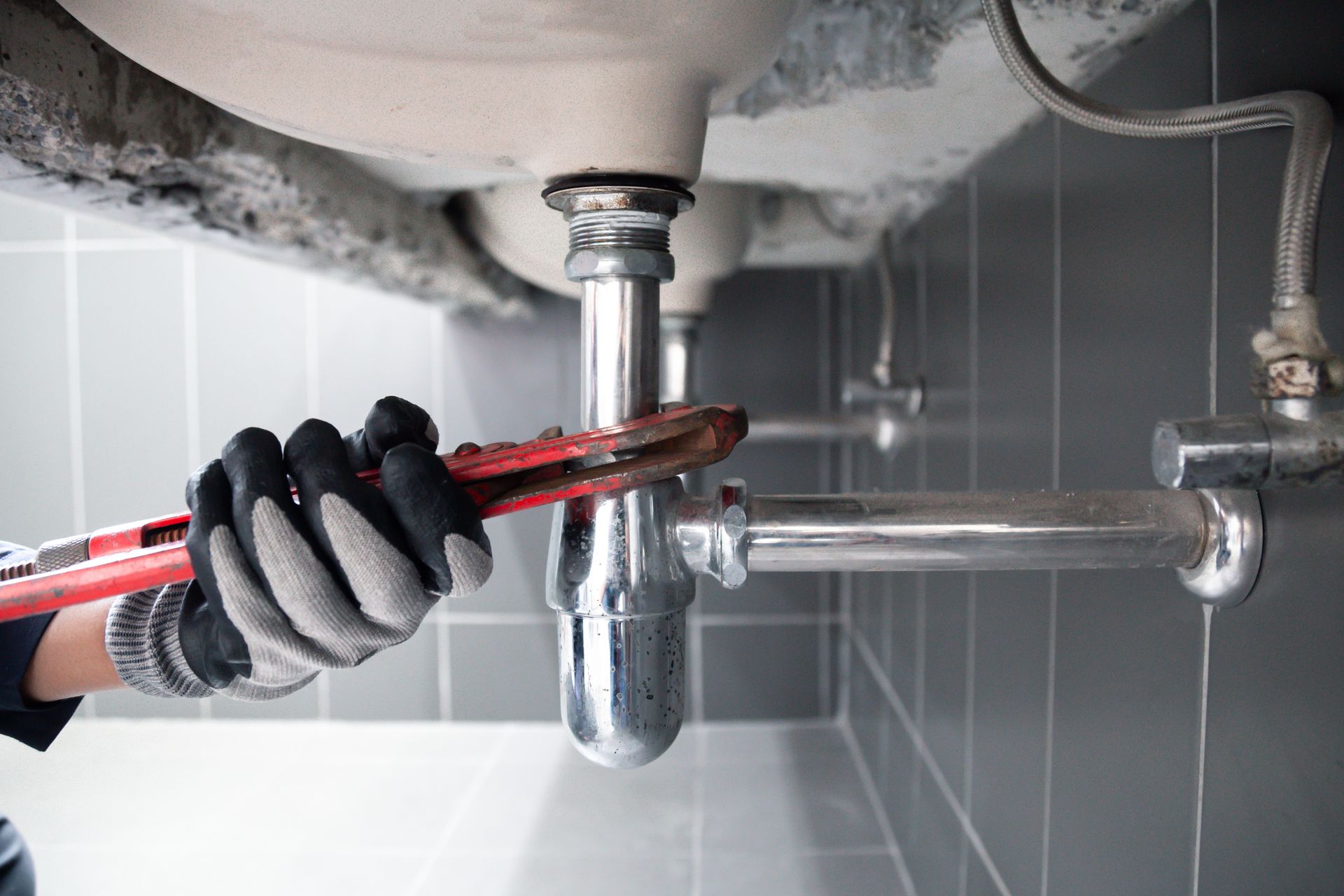 Un plombier resserre le tuyau d'évacuation de l'évier avec une clé rouge sous le lavabo de la salle de bain.