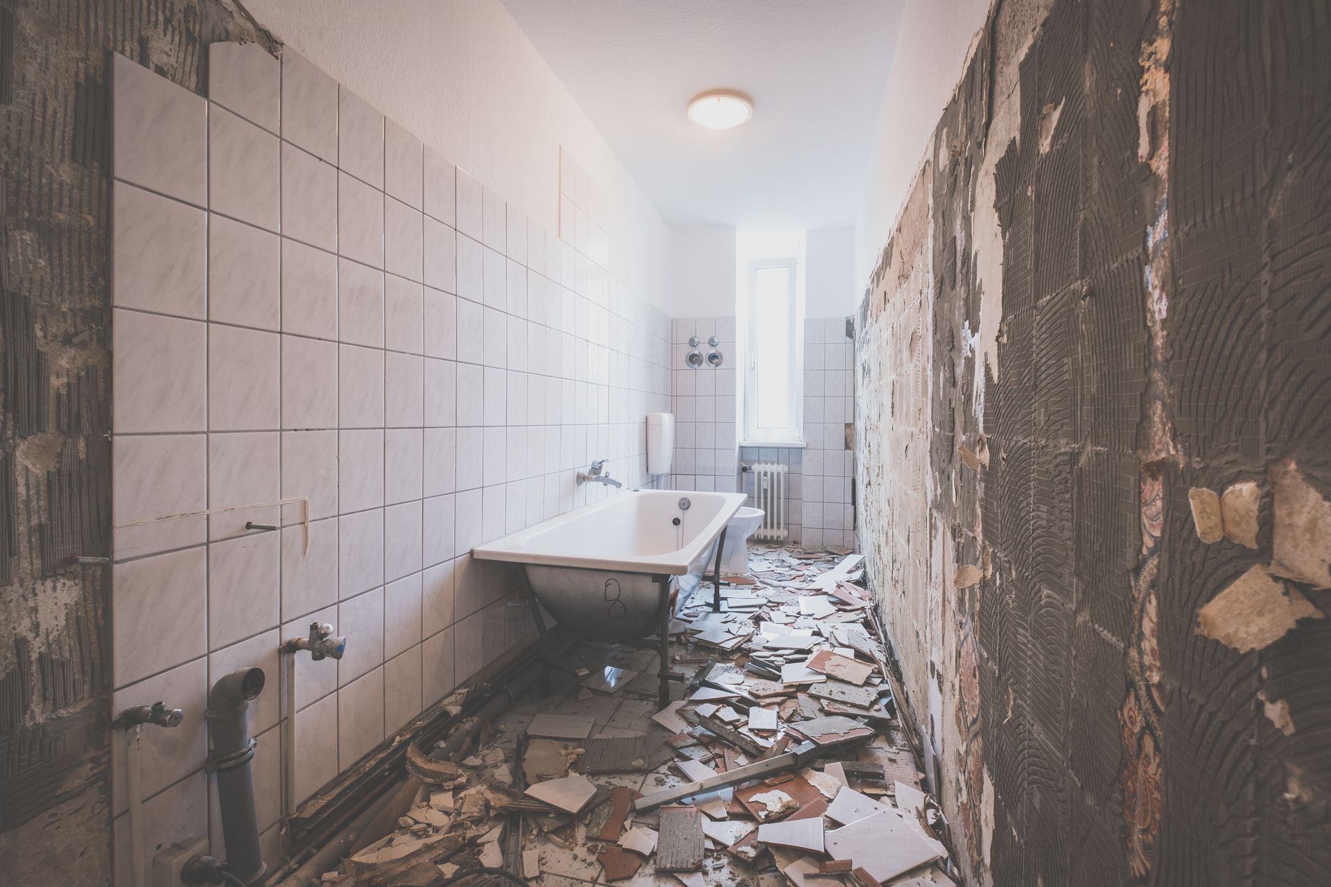 Salle de bains endommagée avec carrelage cassé, débris au sol et lavabo dans une pièce partiellement démolie
