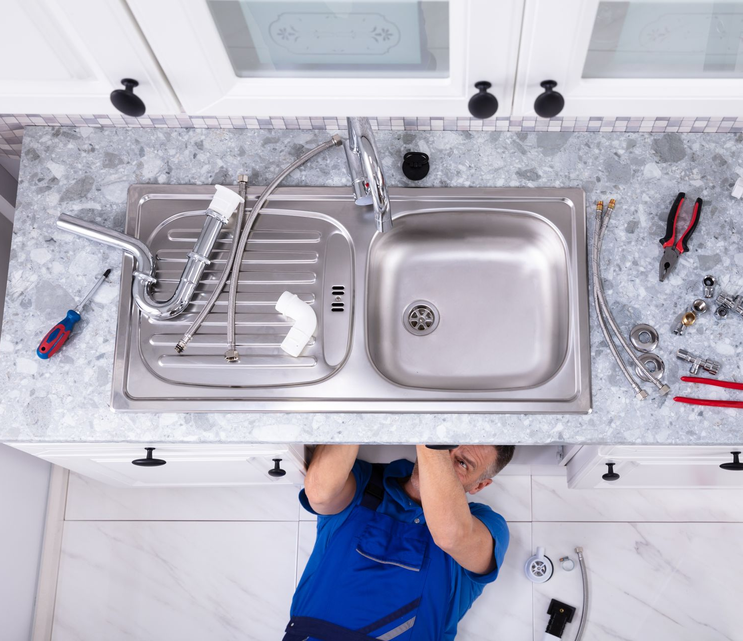 Technicien installant un évier de cuisine en acier inoxydable avec ses outils sur un comptoir blanc