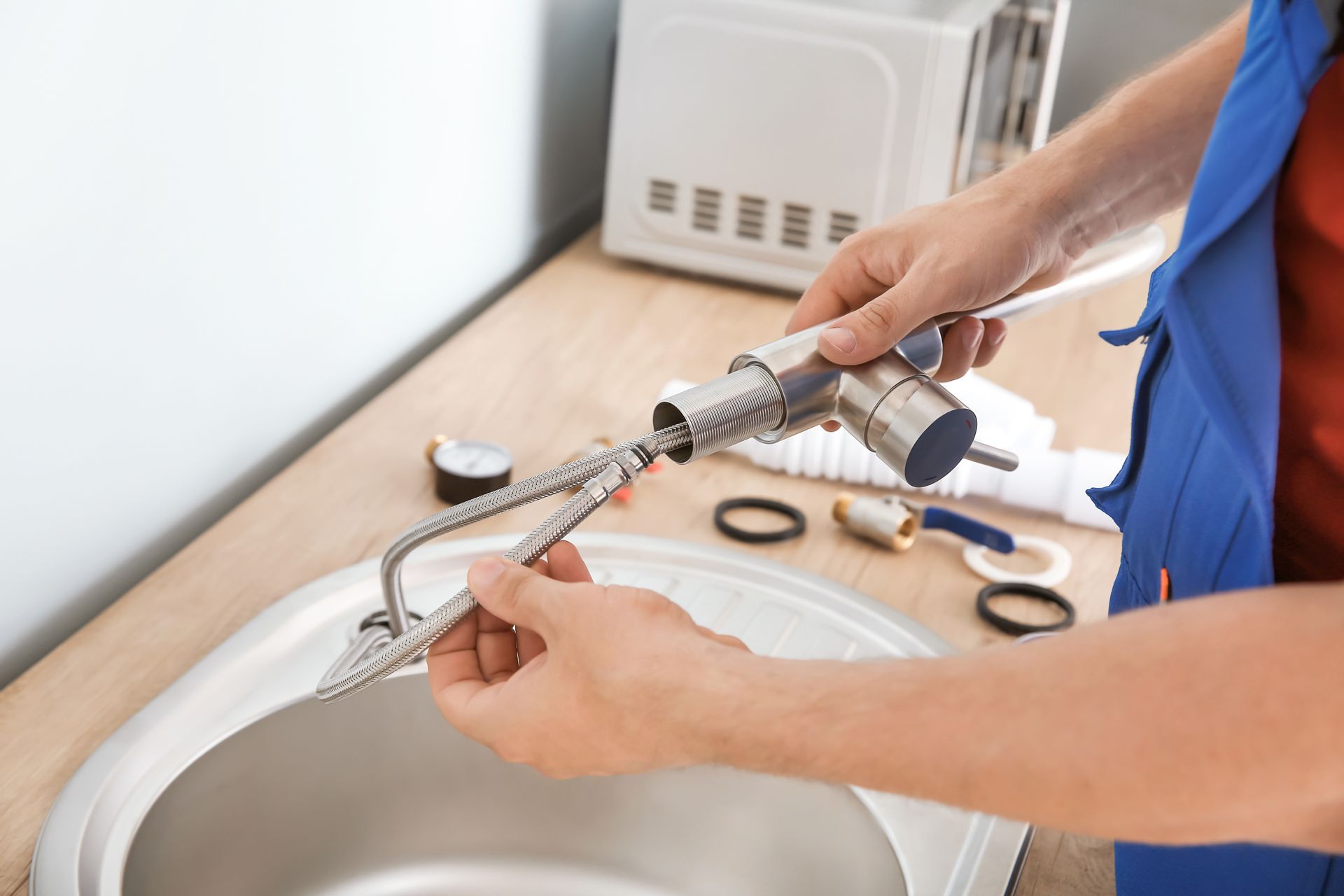 Des mains réparent un robinet d'évier de cuisine avec des outils et des rondelles de rechange à proximité.
