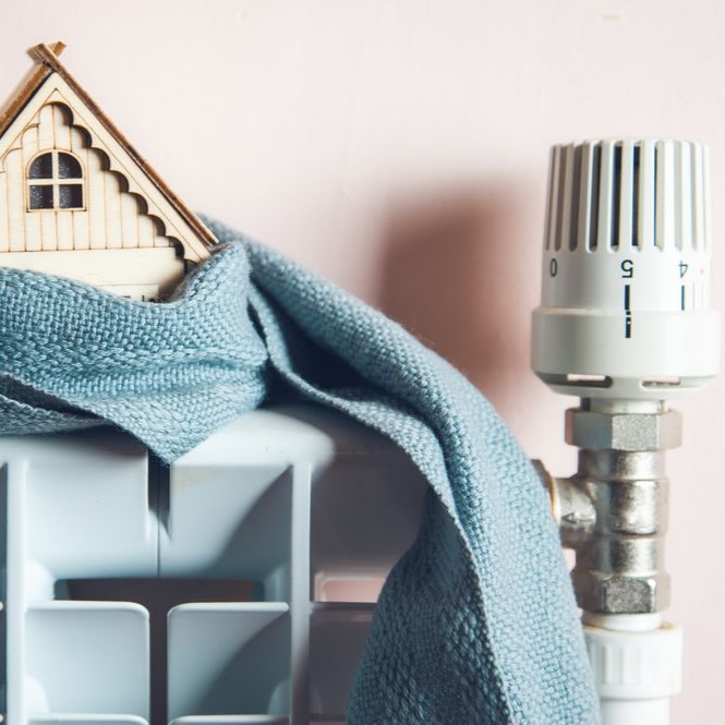Une petite maison sur une étagère bleue à côté d'un bouton de thermostat argenté, avec une douce écharpe bleue drapée dessus.