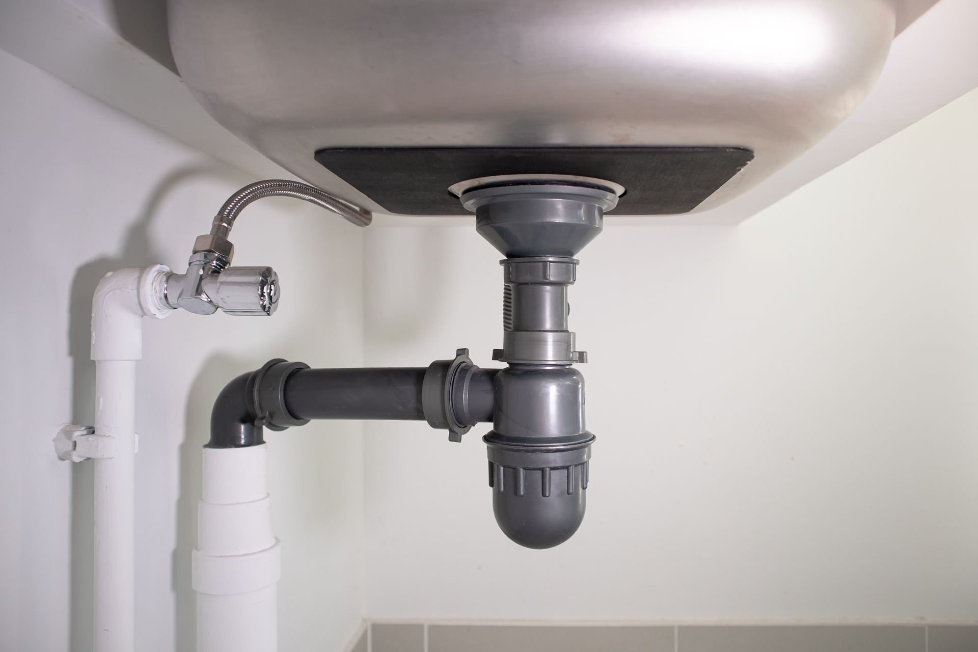 Plomberie sous évier avec tuyaux en PVC gris et siphon sous le lavabo.