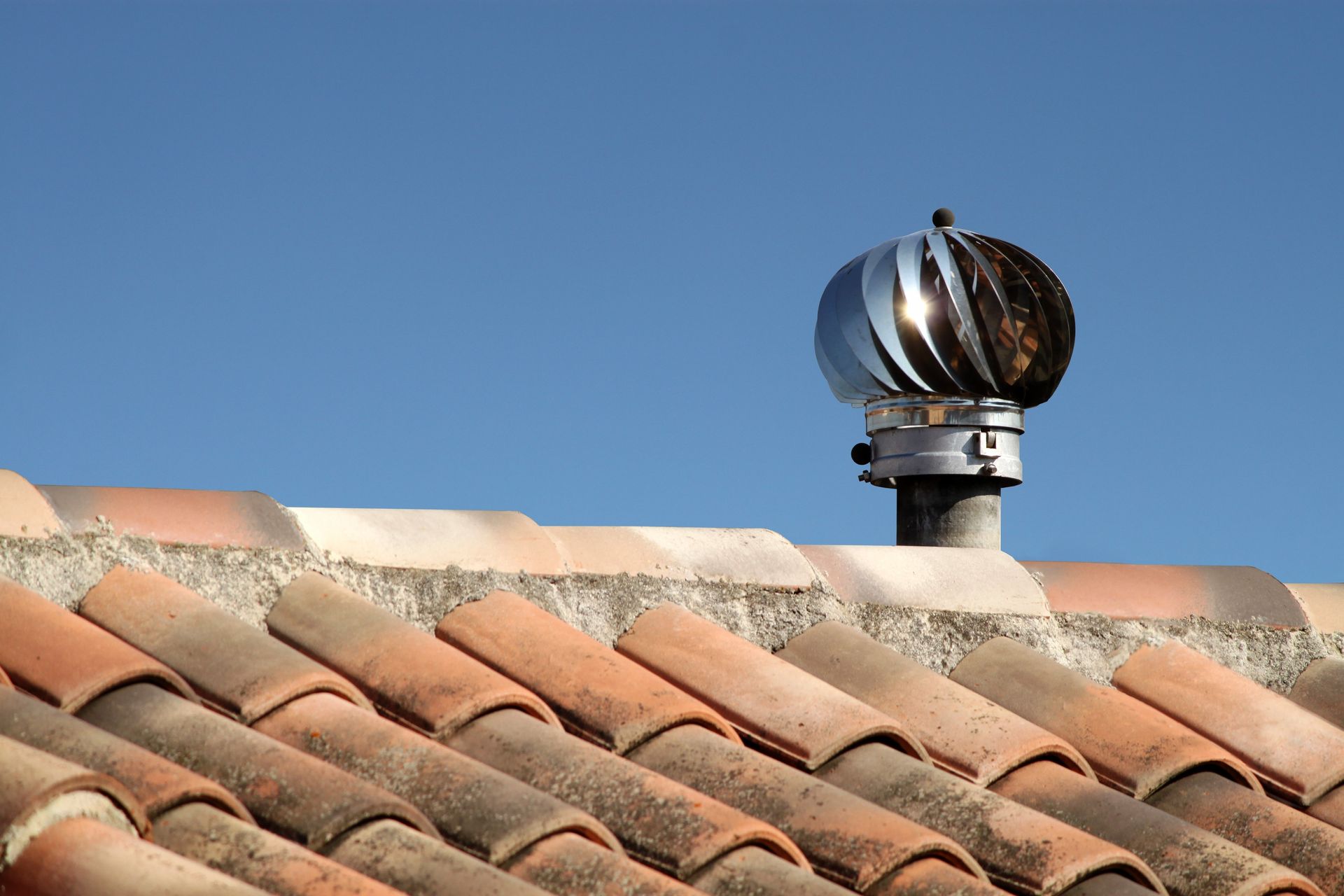 Toiture en tuiles avec une cheminée métallique se détachant sur un ciel bleu clair.