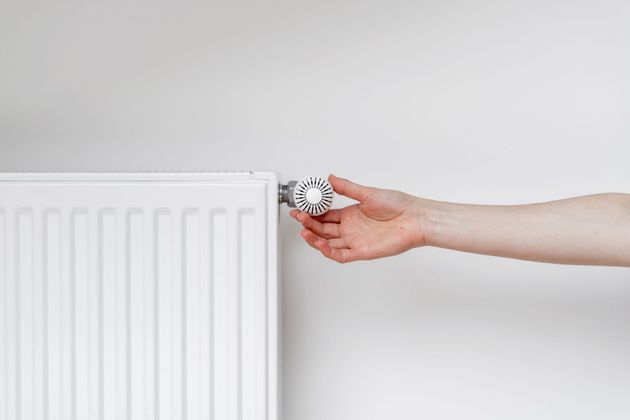 Une main tourne le bouton du thermostat d'un radiateur blanc contre un mur uni