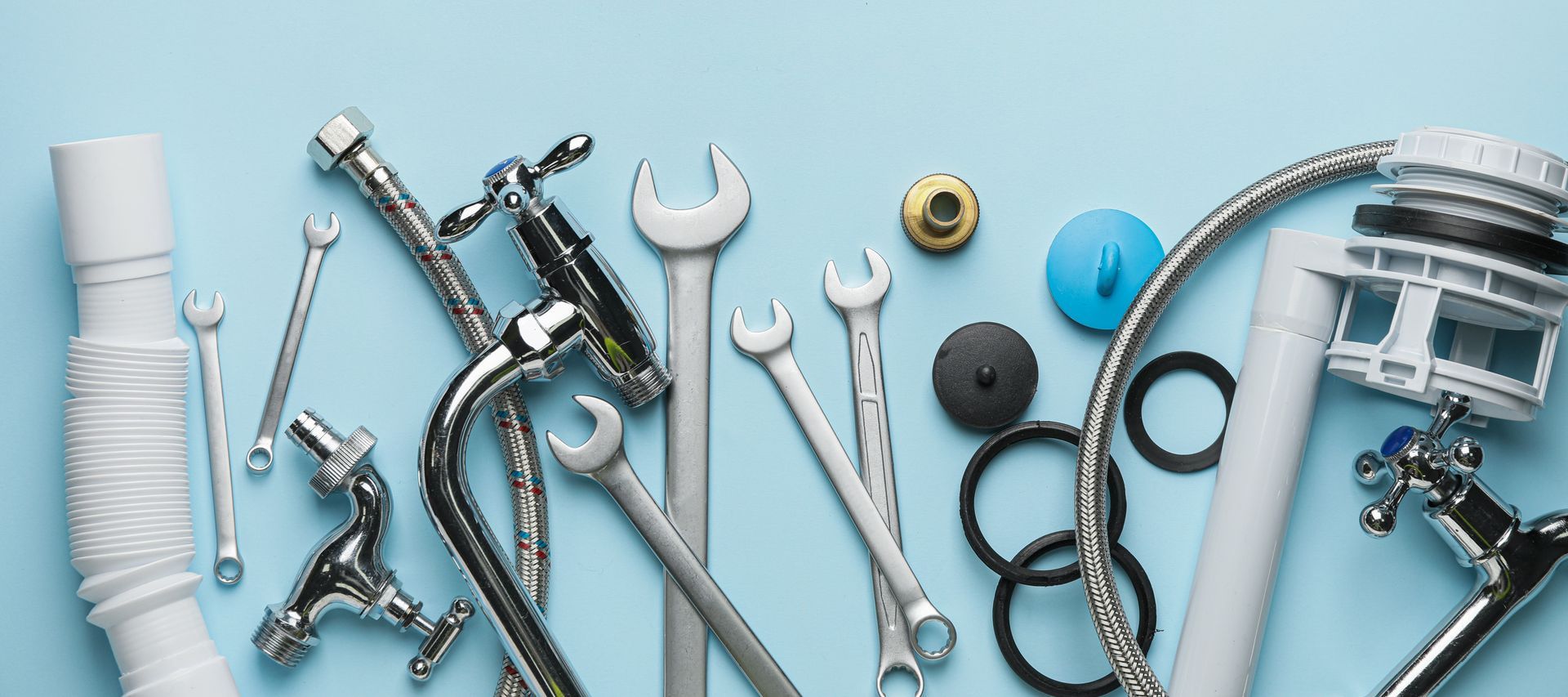 Outils et pièces de plomberie assortis, argentés et bleus, disposés sur une surface bleu clair.