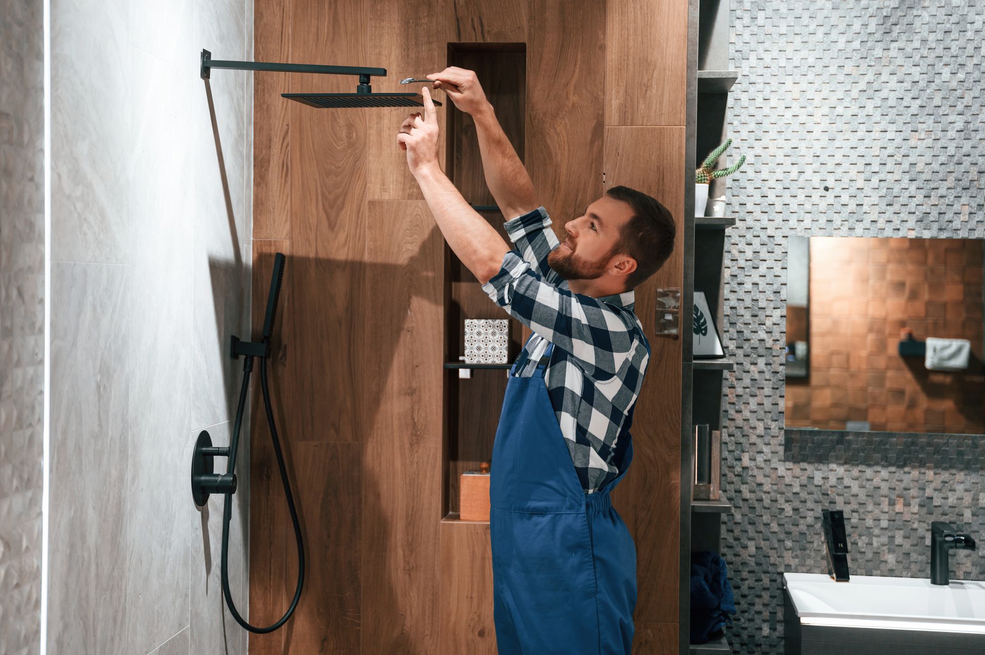 Un ouvrier en salopette bleue installe un support mural pour téléviseur dans une salle de bain moderne