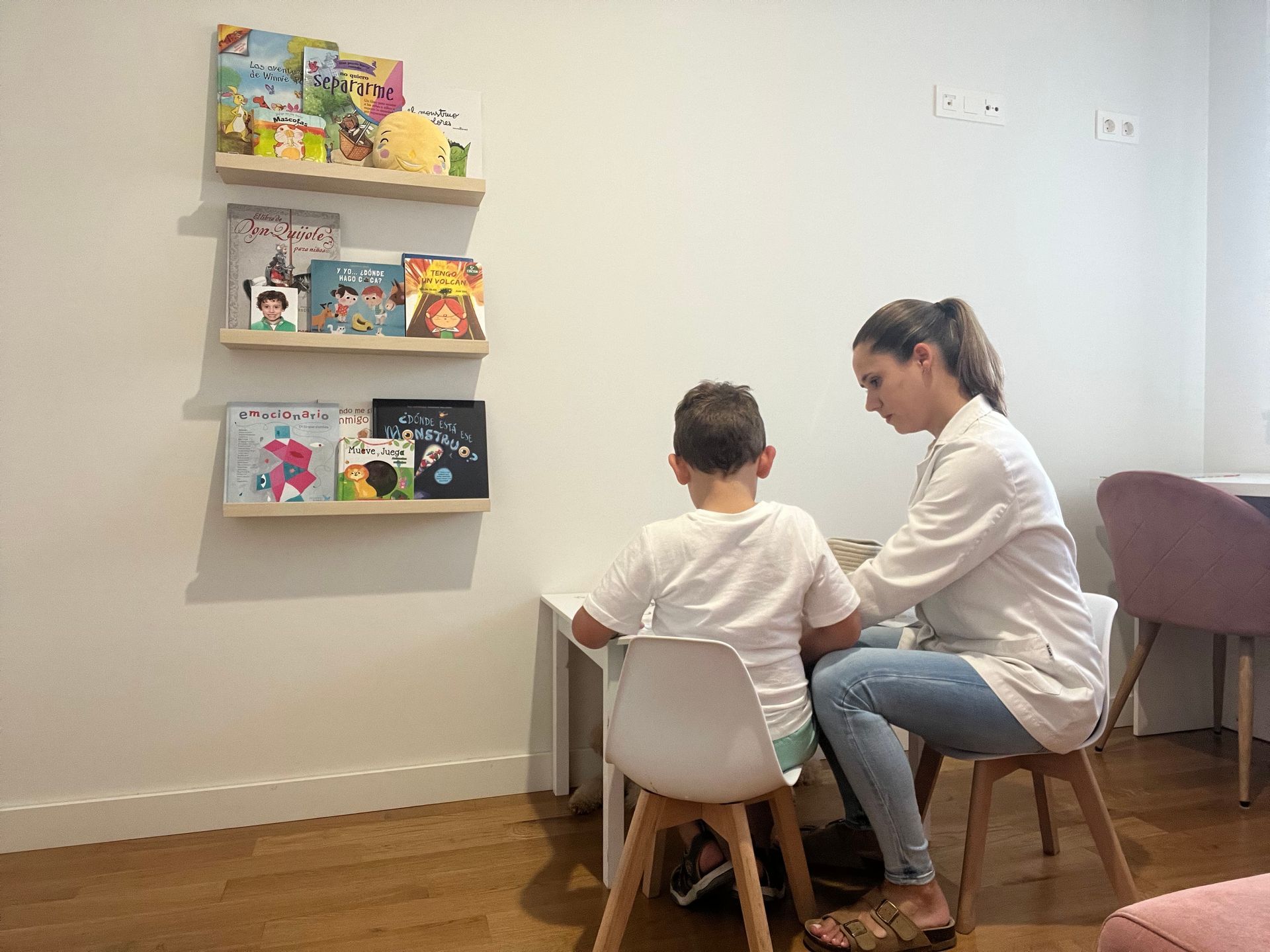 Un niño y un adulto se sientan en una mesa en una habitación con estanterías; están realizando una actividad.