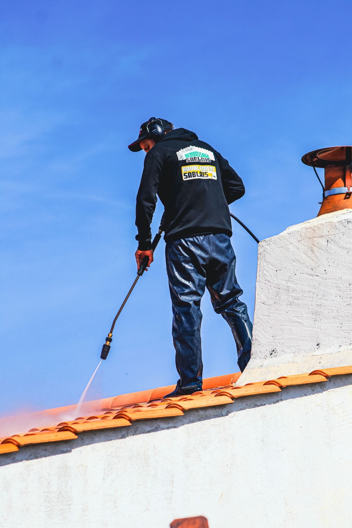 Un artisan muni d'un jet haute pression sur un toit