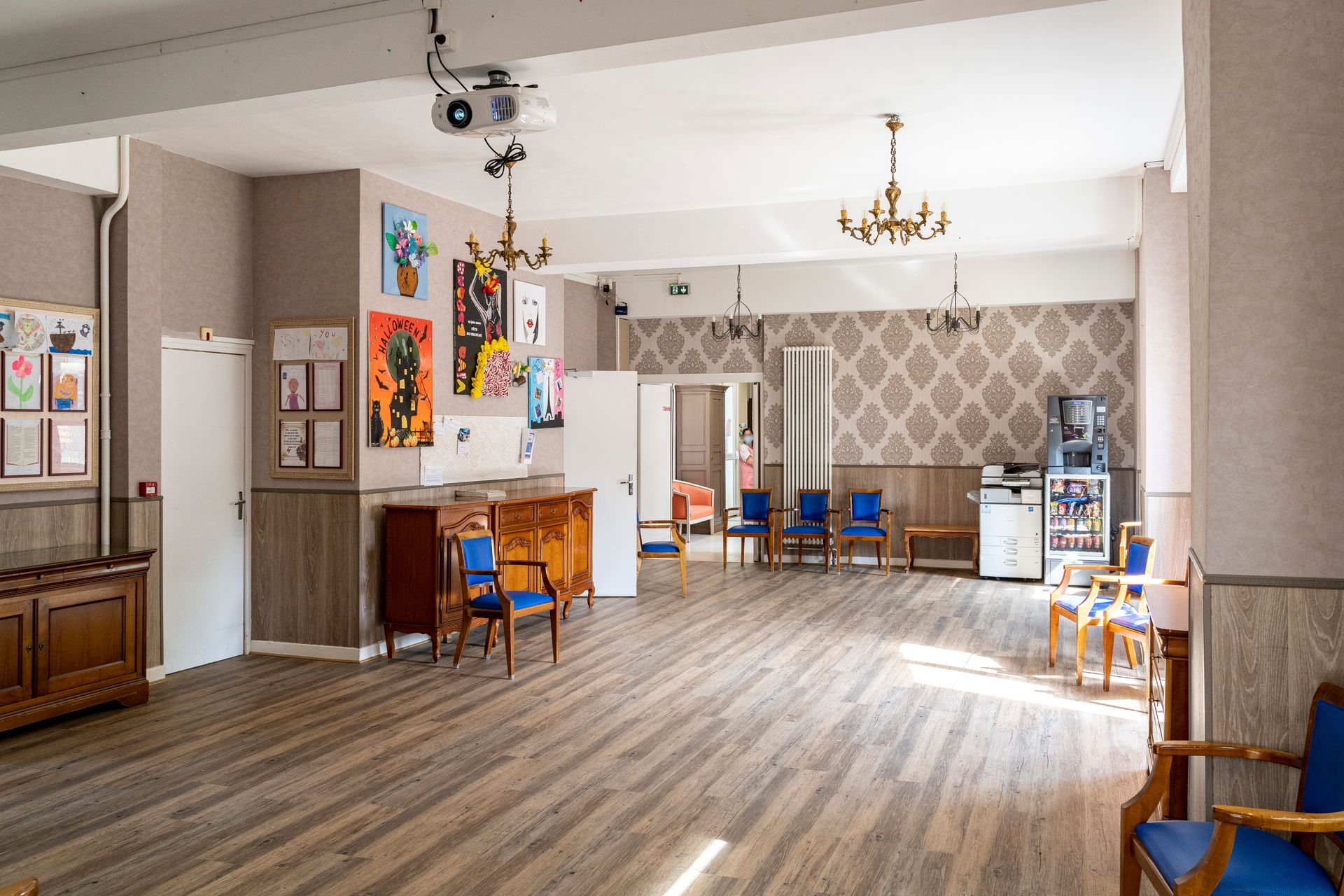 Salle communautaire spacieuse avec parquet, chaises, tables et décorations murales.