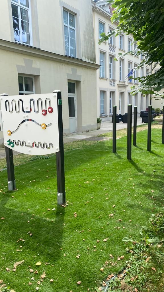Panneau extérieur sur une pelouse à côté d'un bâtiment blanc avec des fenêtres et des arbres à proximité.