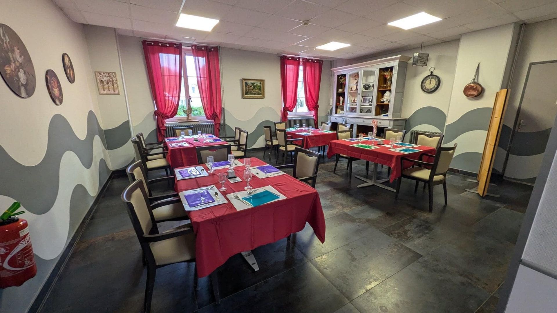 Salle décorée en rouge avec tables, chaises et tableaux, aménagée pour une réunion ou un événement.