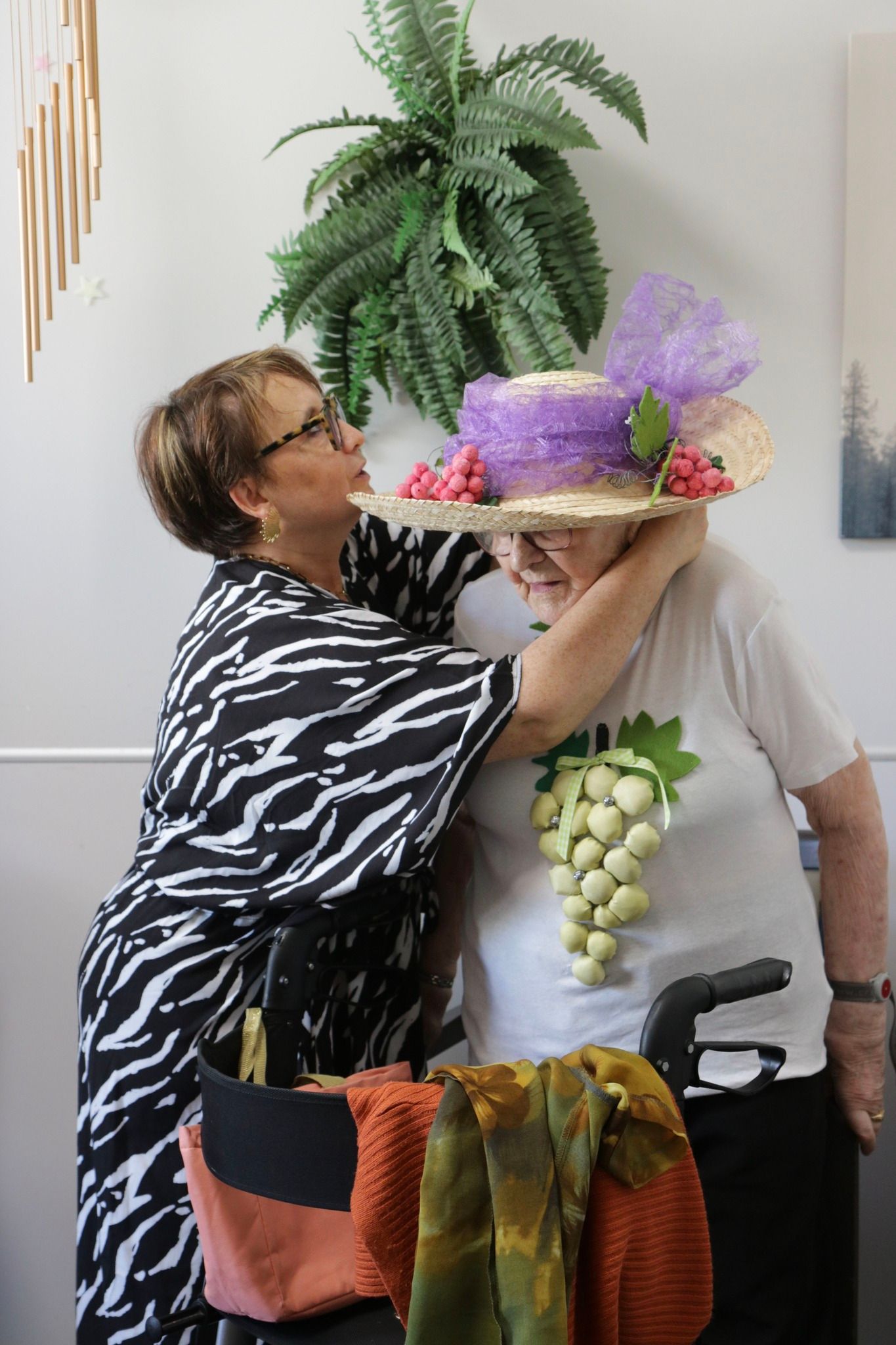 Une personne vêtue d'un costume à imprimé zèbre ajuste un costume coloré à motifs de raisins et de plantes sur une autre personne à l'intérieur.