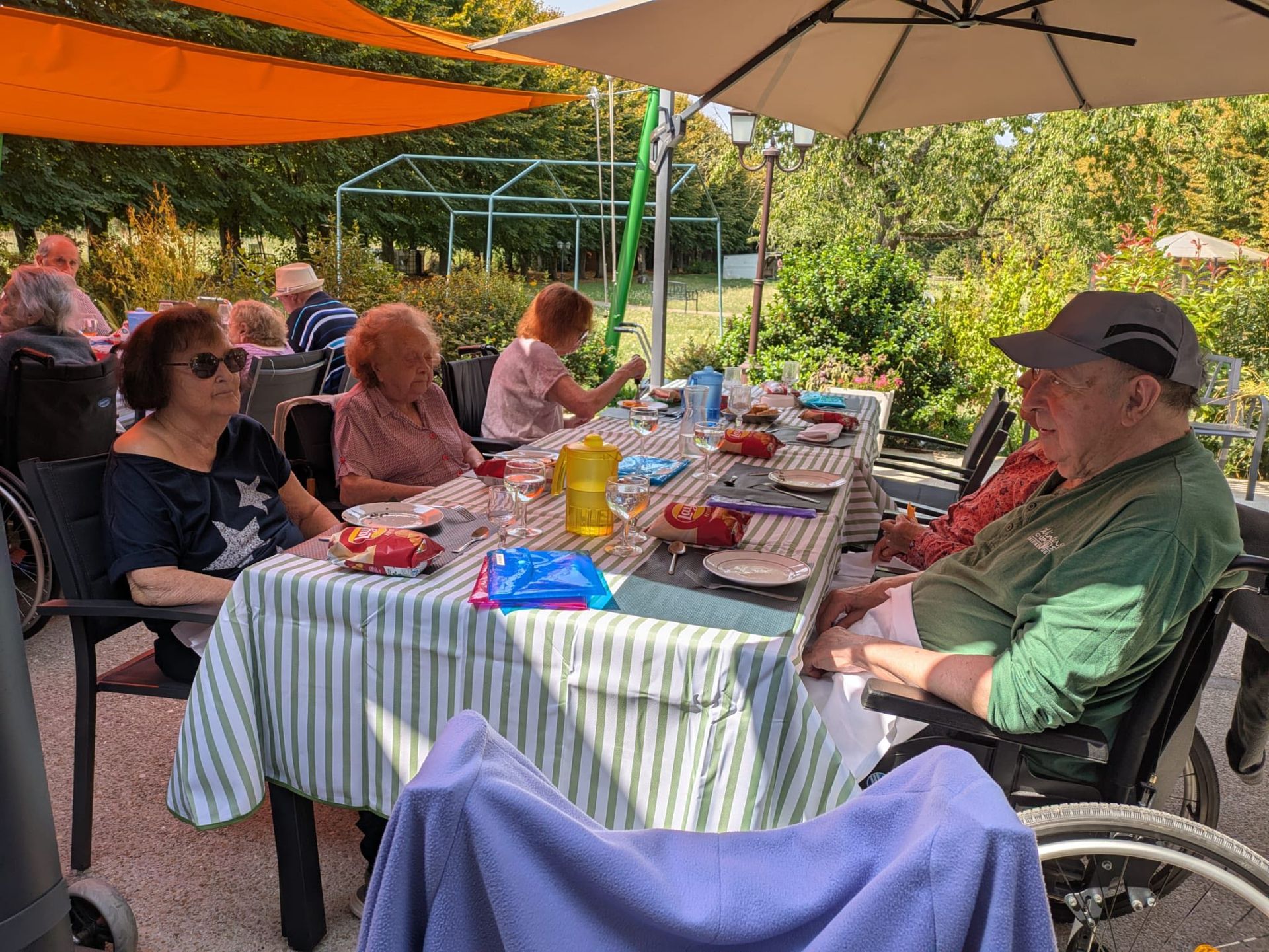 Des personnes assises autour d'une table de pique-nique sous une canopée orange dans un cadre de patio de jardin