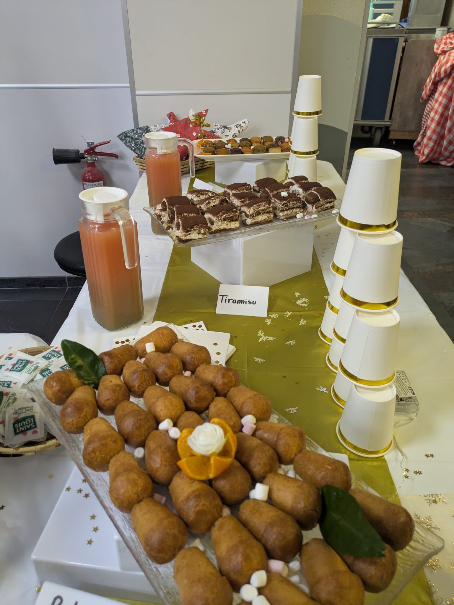 Buffet avec viennoiseries, fruits, bouteilles de jus et gobelets jetables empilés.