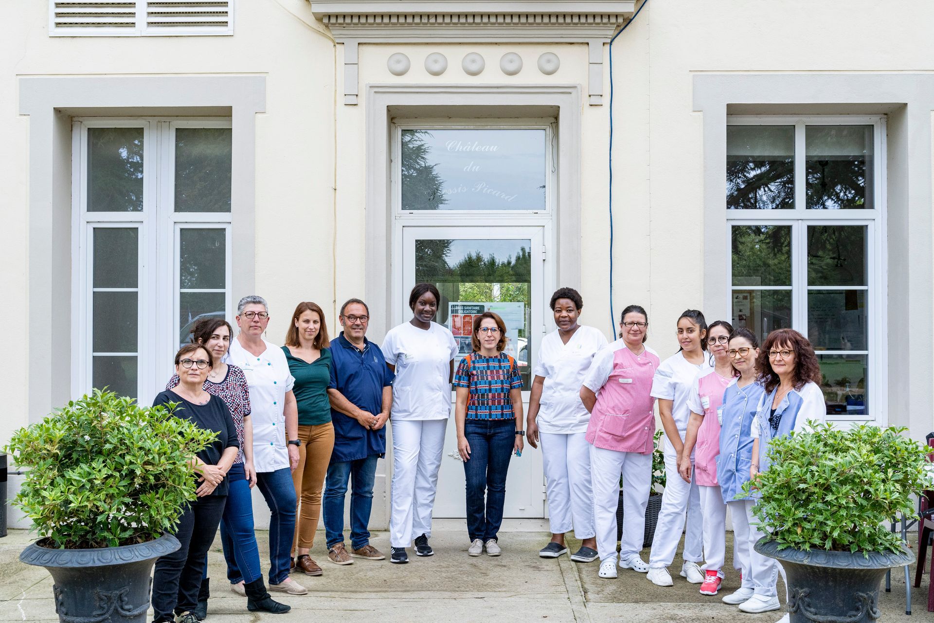Un groupe de personnes pose pour une photo devant l'entrée d'un bâtiment blanc.