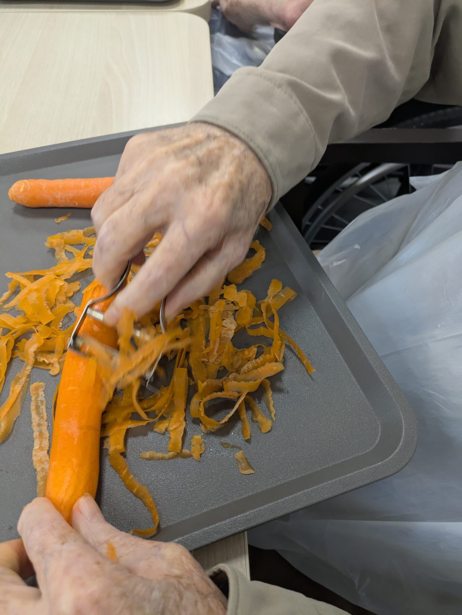 Des mains épluchent des carottes au-dessus d'un plateau recouvert d'écorces d'orange.
