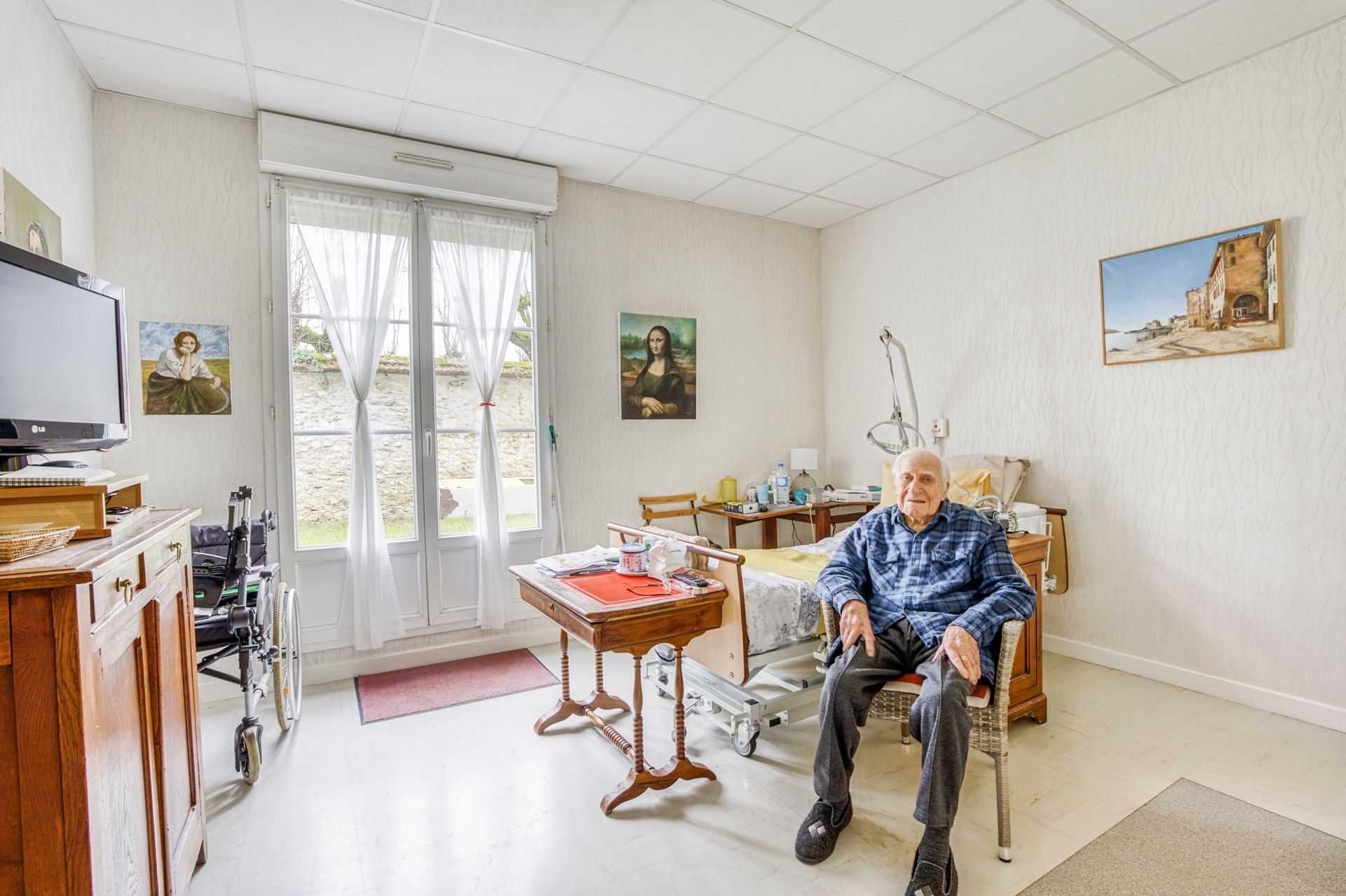Petite salle à manger avec une personne assise, une table, des chaises et de lumineuses portes-fenêtres.