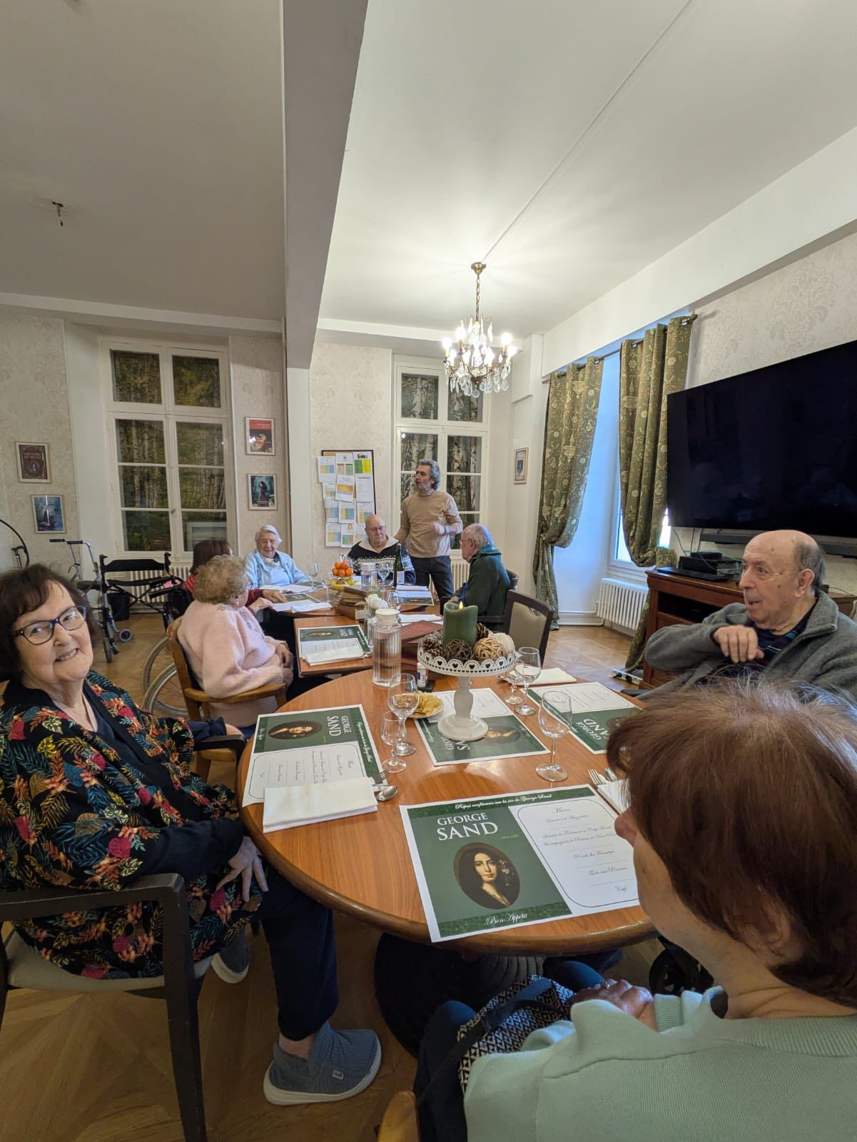 Des personnes assises autour d'une table à manger dans un salon lumineux, avec des papiers et des rafraîchissements, semblaient discuter de quelque chose.