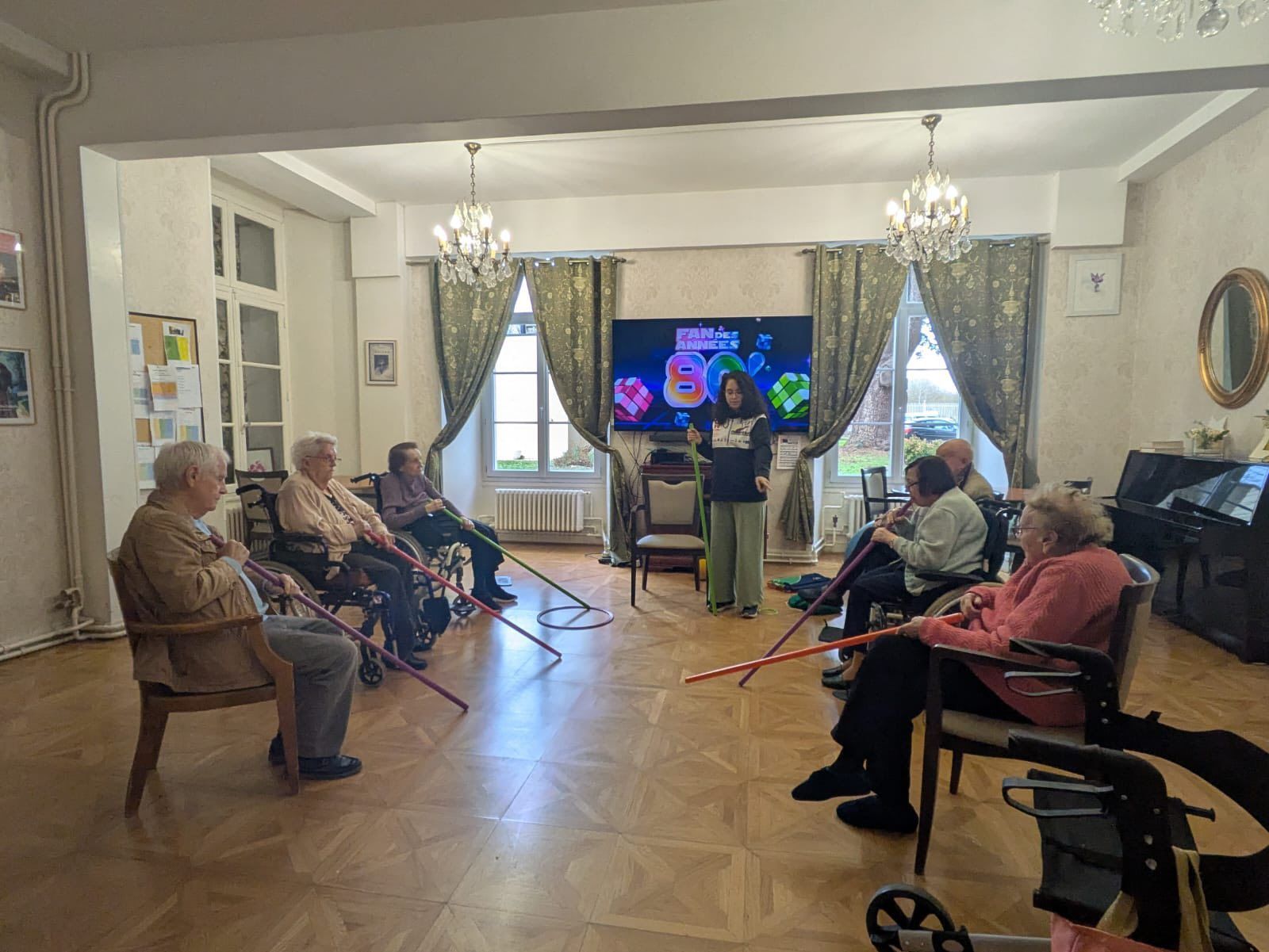 Des personnes assises dans un salon regardent un orateur faire une présentation sur un écran de télévision
